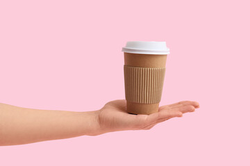 Female hand with disposable cup of coffee on pink background