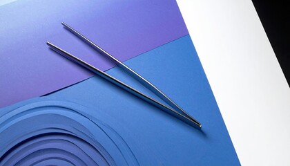 Metallic tweezers laid on layered papers of blue hues and white, in a still-life