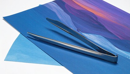 Silver tongs rest on two overlapping sheets of abstract colorful art paper