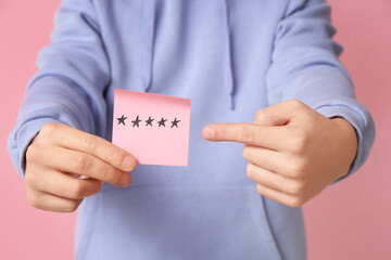 Man pointing at paper with rating stars on pink background, closeup. Survey concept