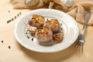 Plate with baked garlic, peppercorns and thyme on light wooden background