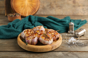 Tray with baked garlic, rosemary and thyme on wooden background