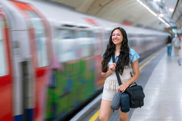 Latina woman smiles joyfully as a train rushes behind her at a London, England underground...