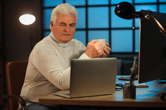 Senior programmer with cup of coffee working in office at night - Powered by Adobe