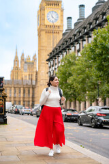 Happy young Latina woman walks near Big Ben and the Houses of Parliament in London, England. Wearing a skirt, turtleneck, smiles as explores one of the most iconic photographed sites in British © Itza