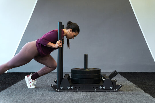 Latin american woman engaging in intense sled push exercise, building strength and endurance at the indoor fitness center