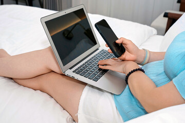 Naklejka premium Person using laptop and mobile phone while sitting on bed