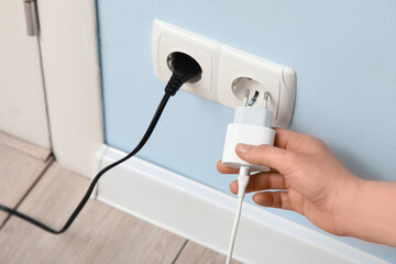 Female hand unplugging charger from socket on blue wall at home, closeup
