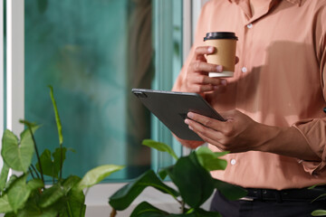 Coffee Break. Professional holding a tablet and coffee cup in a cozy workspace.