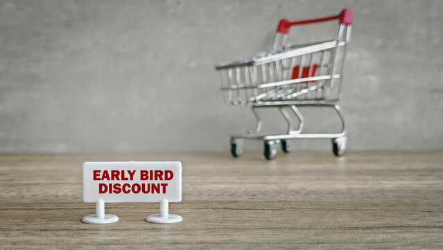 Early Bird Discount or Special Offer Concept: Sign with Red Text and a Miniature Shopping Cart on a Wood Table.