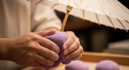 Hands shaping purple dough under a small white umbrella, a culinary art form.