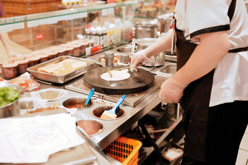 Chef making crepe in a busy food stall with various ingredients around
