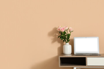 Stylish workspace with modern laptop and beautiful flowers near beige wall