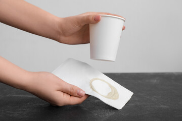 Woman wiping spilled coffee with paper napkin on grunge black table