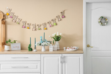 Interior of festive kitchen with flowers and Easter decorations on counter near beige wall