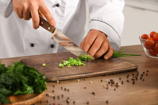 Male chef cutting green onion at table in kitchen, closeup