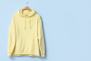 Hanger with stylish yellow hoodie on blue background