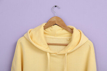 Hanger with stylish yellow hoodie on lilac background, closeup