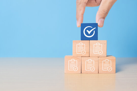Hand holding white correct sign mark on blue wooden block cube and the top of document icon for ISO quality control certification and project approval concept. - Powered by Adobe