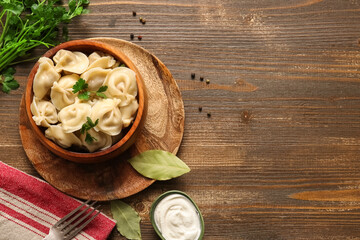 Bowl of delicious boiled dumplings with parsley and sour cream on wooden background