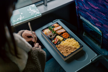 Young Asian woman eating traditional Japanese food lunch box bento while travel on train in winter...