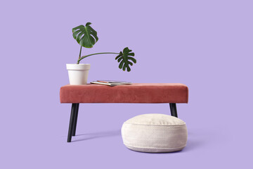 Pink bench with magazines, palm plant and pouf on lilac background