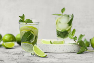 Glasses of fresh Mojito cocktail with limes and mint on grey background