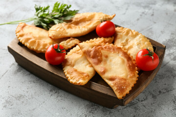 Board with tasty chebureks, tomatoes and parsley on grey grunge table