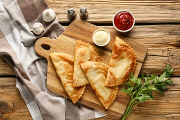 Board with tasty chebureks, fresh parsley and sauces on wooden table