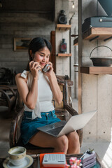 A young woman multitasks with a phone and laptop in a cozy, modern cafe environment, showcasing productivity and technology.