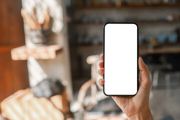 Close-up of a hand holding a smartphone with a blank screen in a cozy cafe, ideal for mockups or design presentations.
