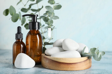 Wooden bowl with spa stones, eucalyptus twig and bottles of cosmetic products on blue grunge background, closeup