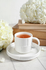 Beautiful hydrangea flowers with cup of tea and books on tile table against light wall