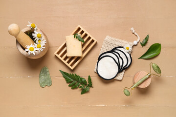 Bag, reusable cotton pads, soap bar and green leaves on beige wooden background