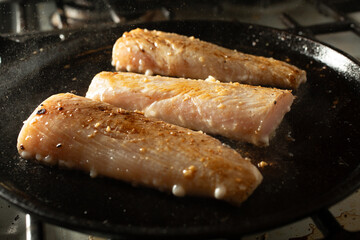 A view of three mahi mahi fillets cooking on a cast iron comal, on the stove.