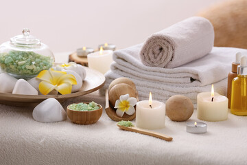 White couch with plumeria flowers, clean towels and burning candles in bathroom, closeup