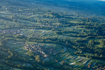 Aerial view of lush green rice terraces and a small village nestled in a valley, bathed in soft morning light.