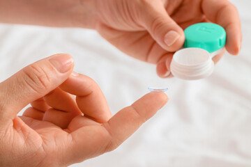 Young woman holding contact lens on finger at home, closeup