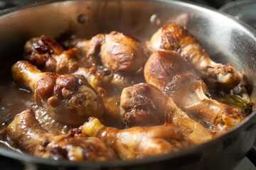 A view of chicken adobo cooking in a wide shallow pot.
