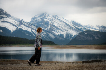 Naklejka premium Lone wanderer by serene lake, majestic snow-capped mountains.