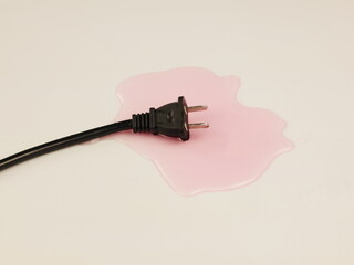 A black electrical plug immersed in a puddle of liquid on a light-colored surface.