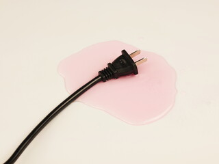 A black electrical plug immersed in a puddle of liquid on a light-colored surface.