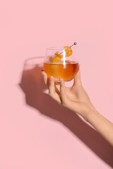 Female hand with glass of tasty Old Fashioned cocktail on pink background