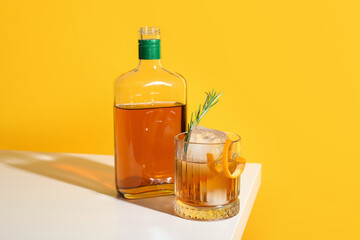 Glass of tasty Old Fashioned cocktail with rosemary on white table against yellow background