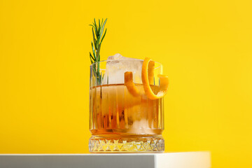 Glass of tasty Old Fashioned cocktail with rosemary on white table against yellow background