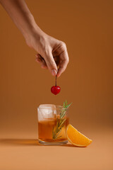 Woman decorating glass of tasty Old Fashioned cocktail on brown background