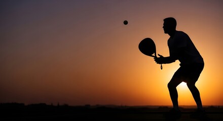 Dramatic silhouette of a male padel player in action, preparing to hit the ball with his racket against a vibrant, golden sunset sky background