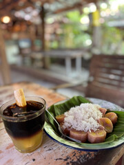 Traditional Indonesian banana snack with grated coconut and herbal drink. Authentic Indonesian banana roll with grated coconut served on banana leaf, paired with refreshing herbal drink