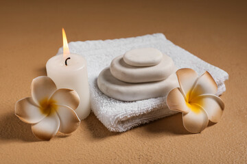 Spa composition with plumeria flowers, towel, stones and candle on yellow grunge background, closeup