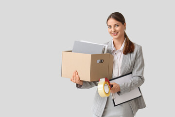 Young happy businesswoman holding cardboard box with belongings, folders and packing tape dispenser...